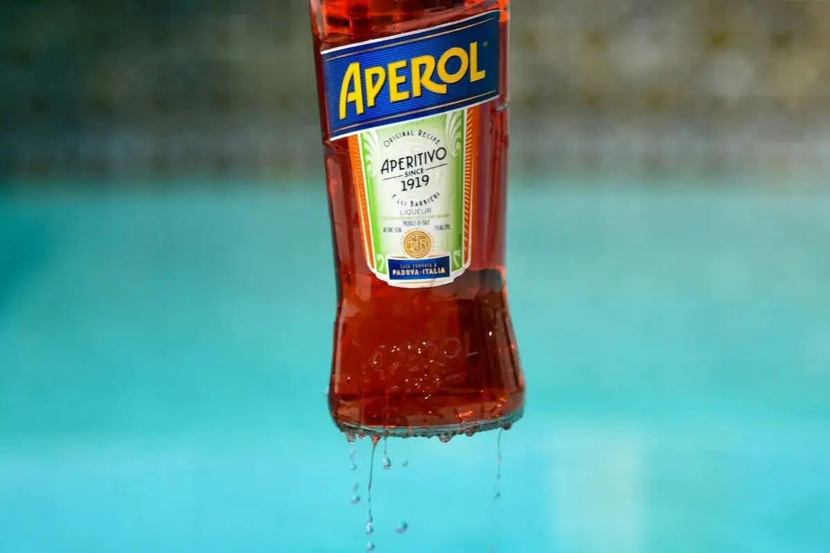 Aperol, czyli gorzki włoski likier, kapie z butelki na tle basenu.
