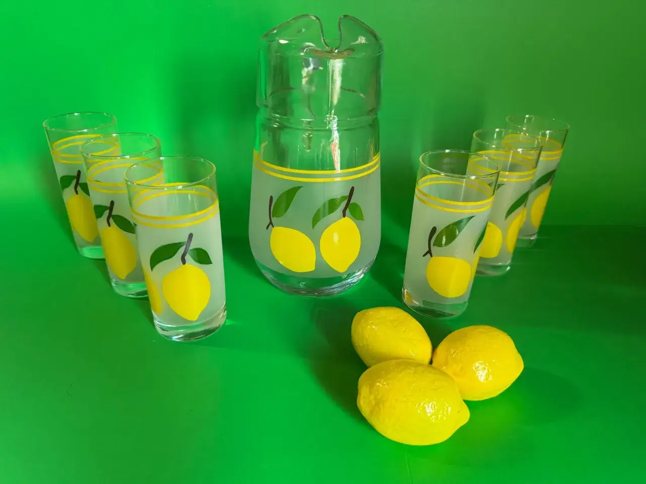Service &agrave; bi&egrave;re citron nom, avec un pichet et six verres d&eacute;cor&eacute;s de citrons jaunes et de feuilles vertes. Trois citrons frais sont pos&eacute;s devant.