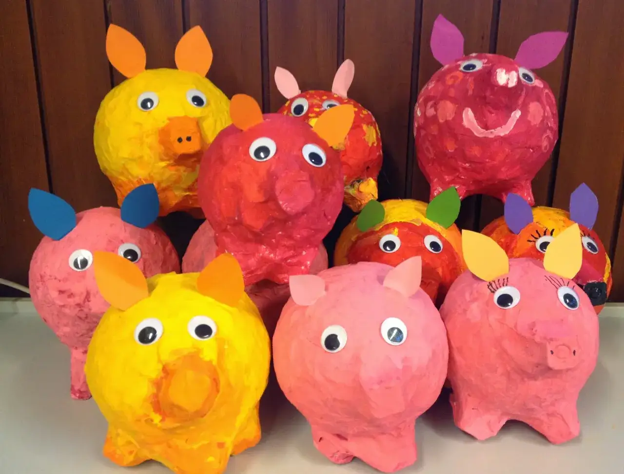 Bunte Luftballon Pappmache Tiere, hauptsächlich Schweinchen, mit großen Kulleraugen und Papierohren, stehen fröhlich nebeneinander.