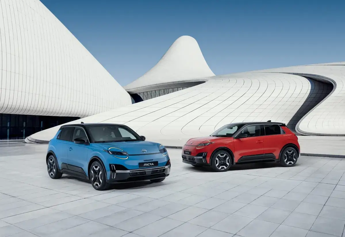 Dwa samochody Nissan Micra, niebieski i czerwony, na tle nowoczesnej architektury. Poznaj nissan micra wymiary i możliwości tego miejskiego auta.