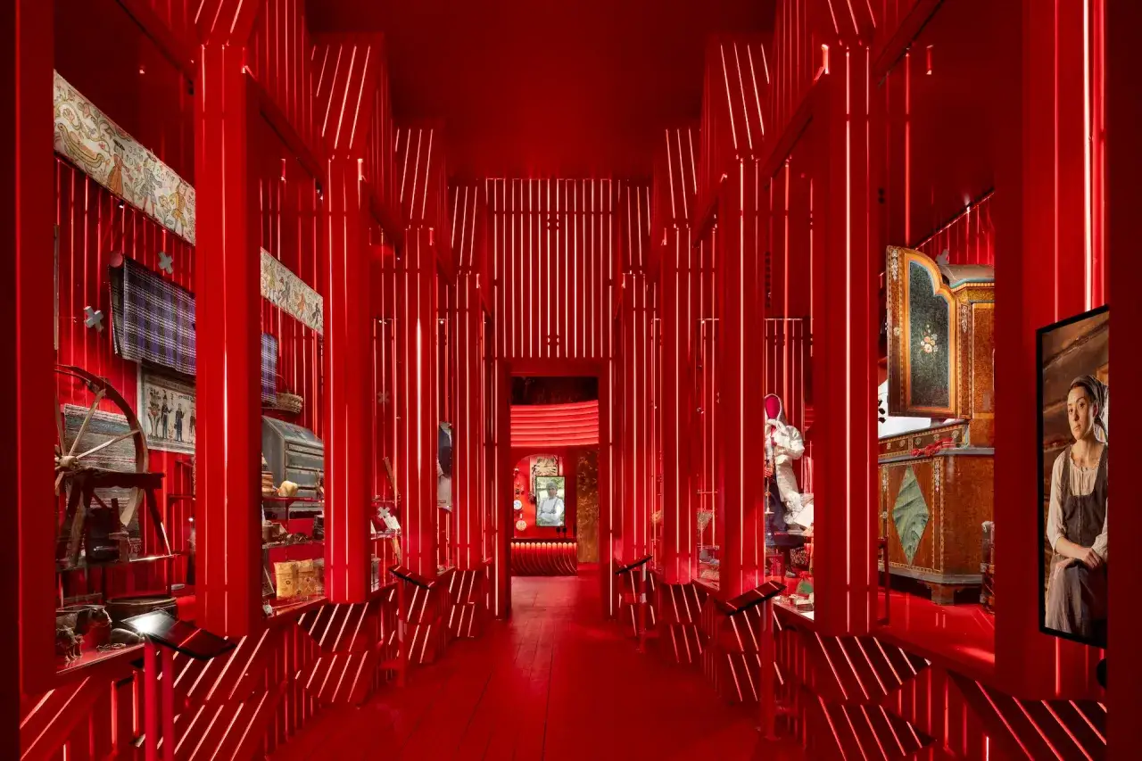 En röd, futuristisk utställning på Nordiska museet med föremål som en gammal spinnrock och målade möbler.