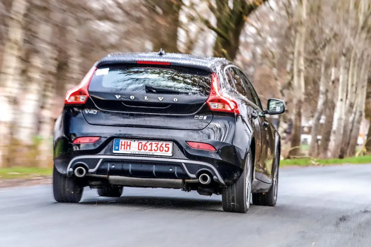 Schwarzer Volvo V40 fährt auf einer Straße, umgeben von Bäumen.