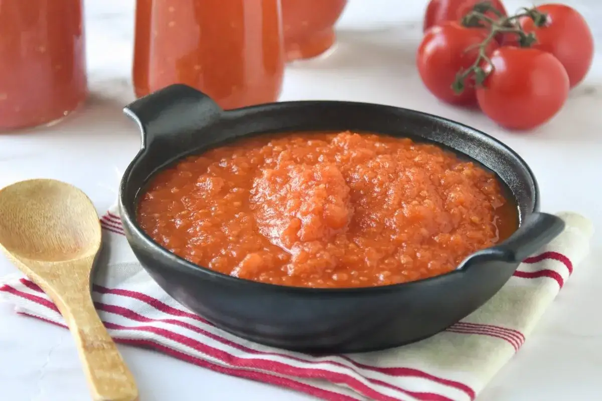Un cuenco negro contiene una generosa porción de passata de tomate casera, lista para usar. Una cuchara de madera descansa a su lado.