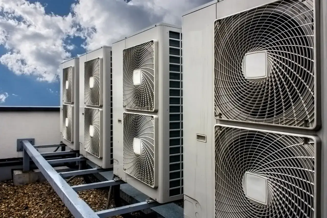Rząd jednostek klimatyzacyjnych na dachu pod błękitnym niebem z chmurami.