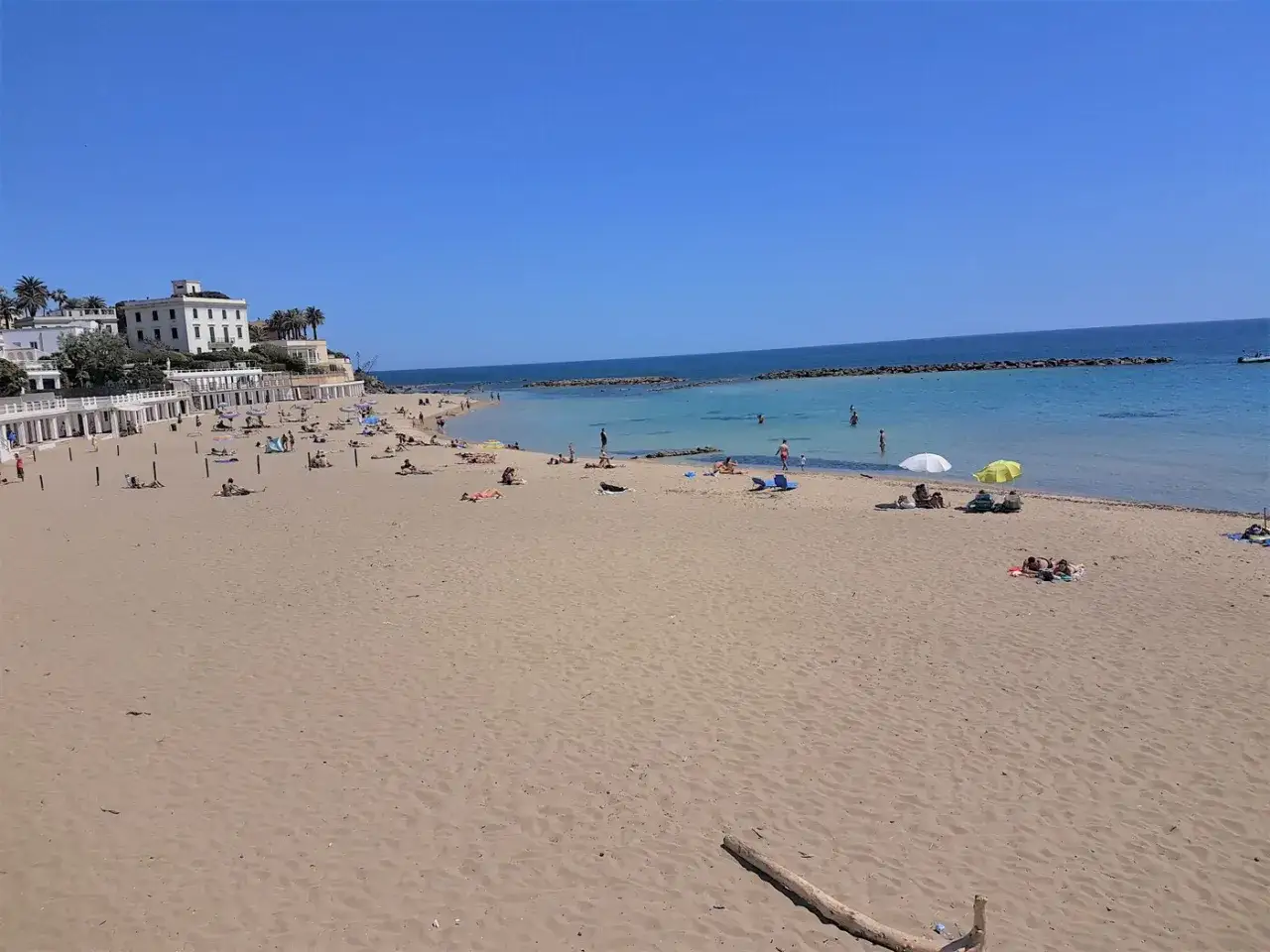 Sonniger Santa Marinella Strand mit vielen Badegästen, Liegestühlen und Sonnenschirmen. Das Meer ist ruhig und blau.