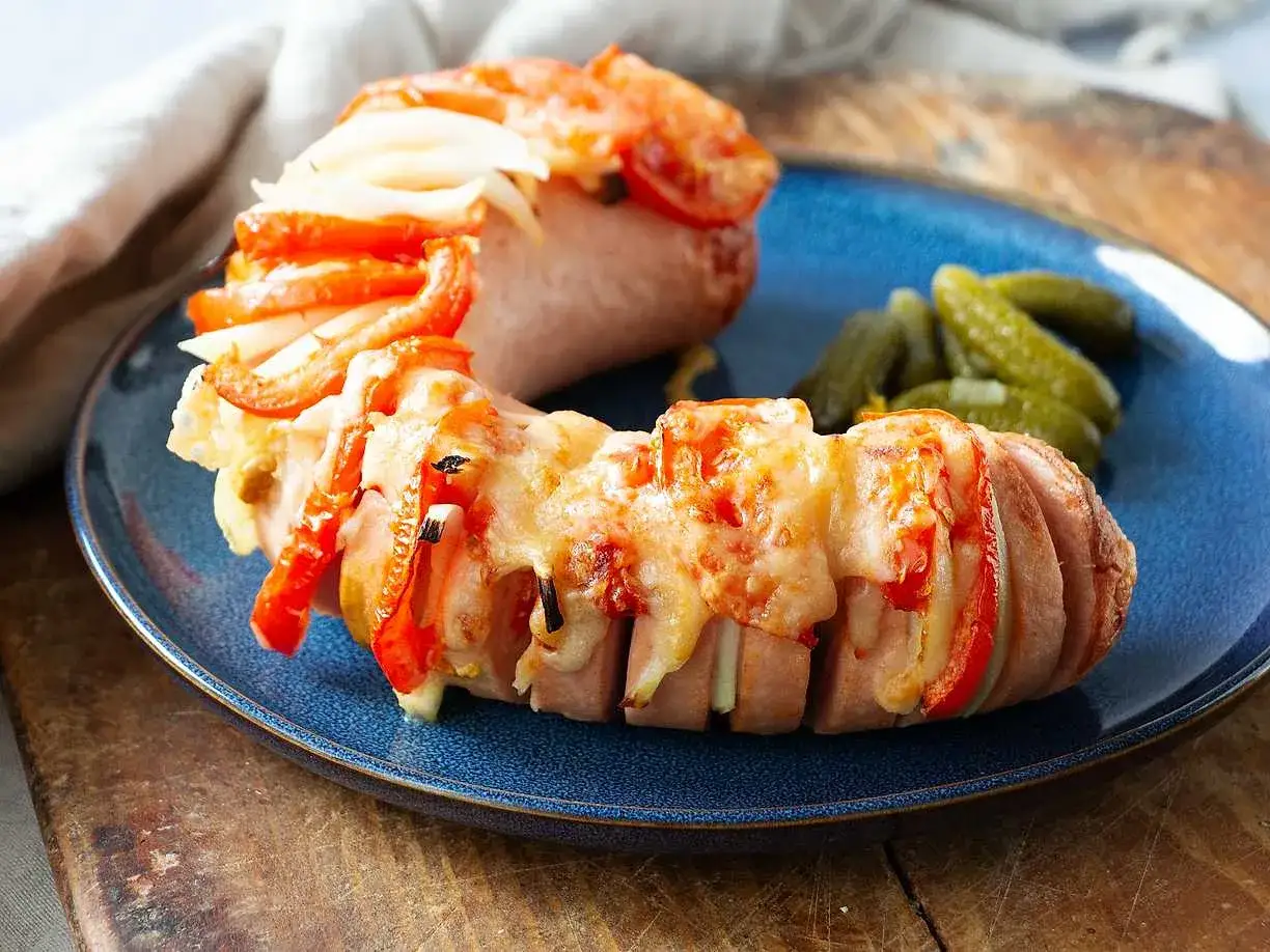 Falukorv i airfryer med ost, paprika och l&ouml;k. Serveras med cornichoner p&aring; en bl&aring; tallrik.