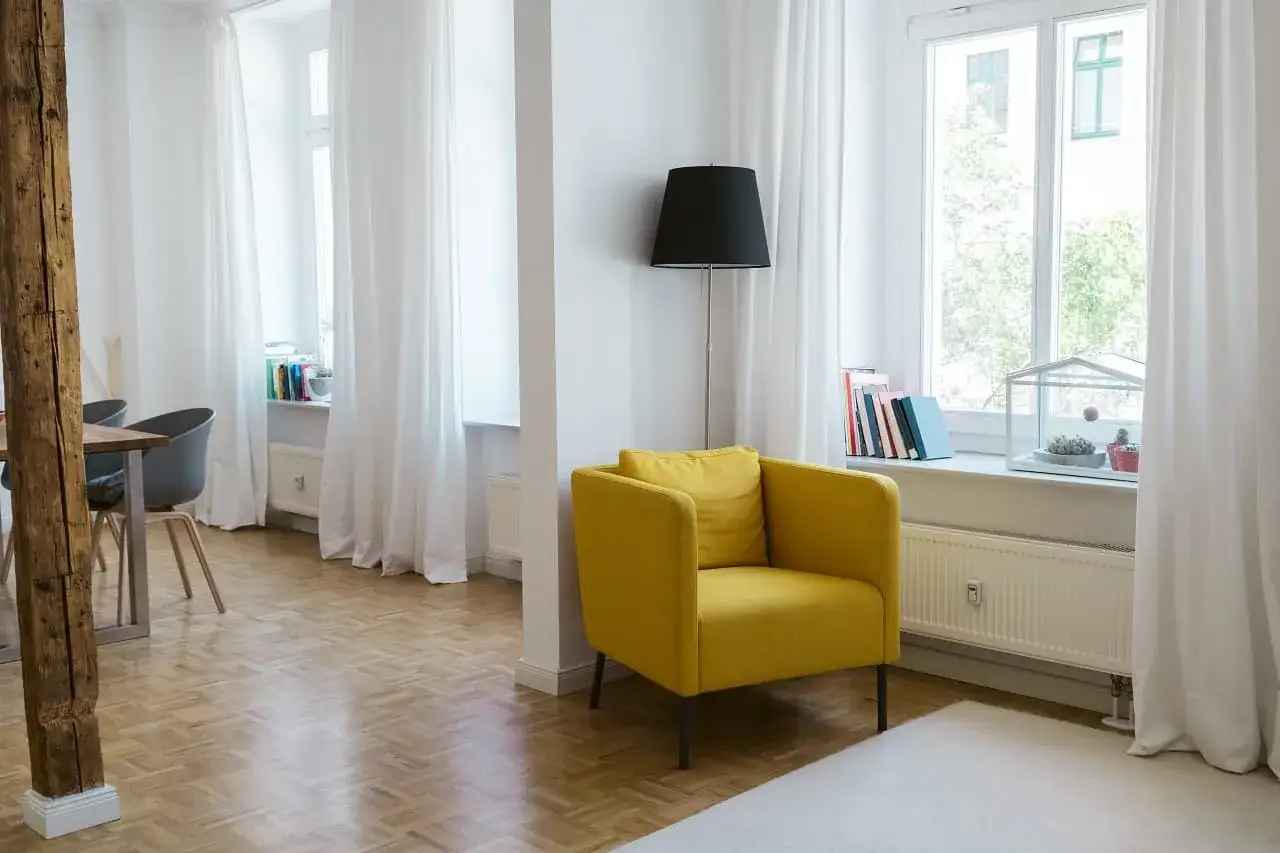 Jasny salon z żółtym fotelem i książkami na parapecie. Dowiedz się, jak ubezpieczyć mieszkanie w bloku.