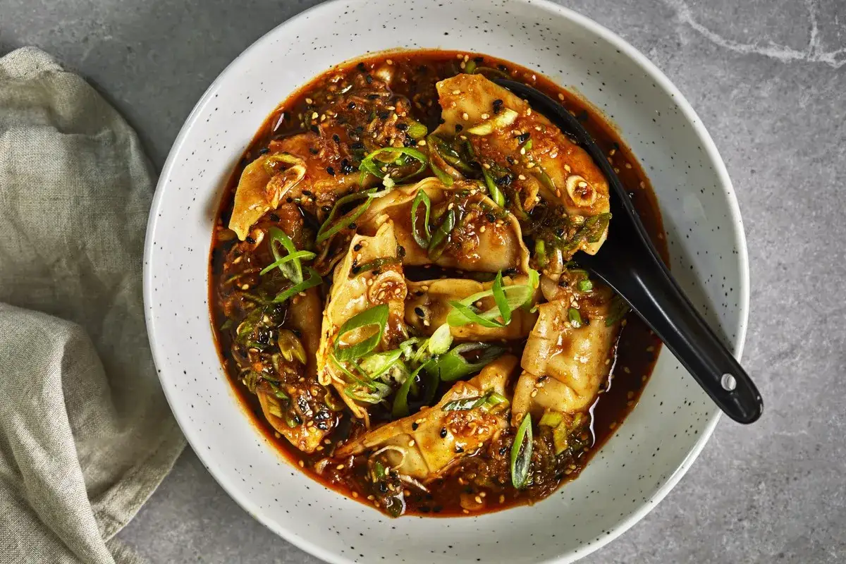 En sk&aring;l med dumplings i en kryddig s&aring;s, toppad med salladsl&ouml;k och sesamfr&ouml;n. Ett perfekt lunch recept f&ouml;r en smakrik m&aring;ltid.