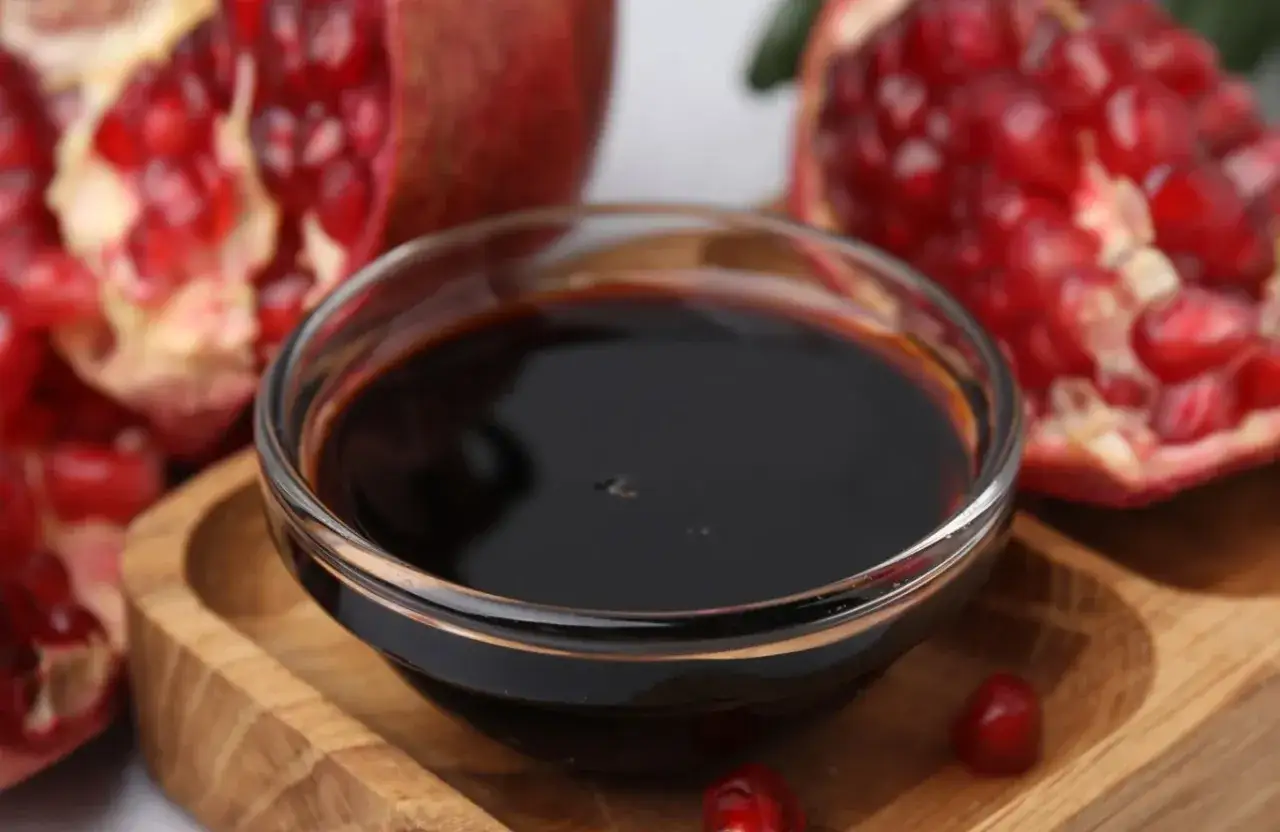 Gęsty, ciemny syrop z granatu w szklanej miseczce, obok połówki owocu granatu.