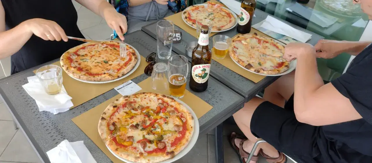 Na stole leżą trzy pizze i piwo. Na rachunku widać cenę 25. Ile kosztuje pizza we Włoszech?
