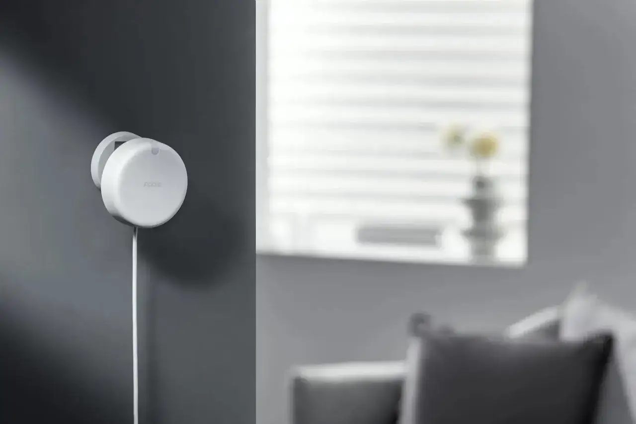 Detector de presencia blanco montado en pared, mostrando c&oacute;mo funciona un detector de presencia para automatizar tu hogar.