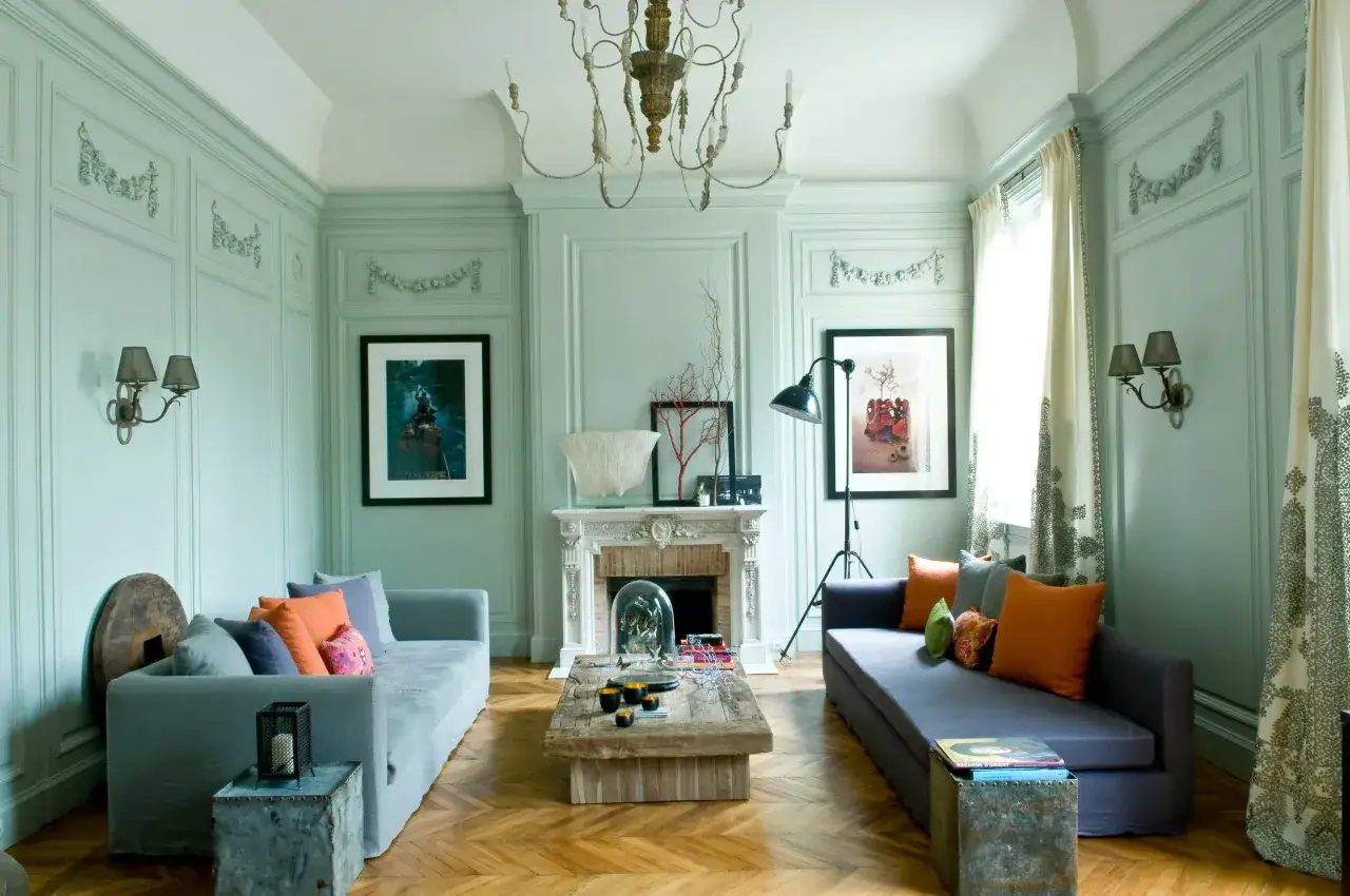 Sofá gris con cojines en gama colores calidos, chimenea de mármol y suelo de madera.