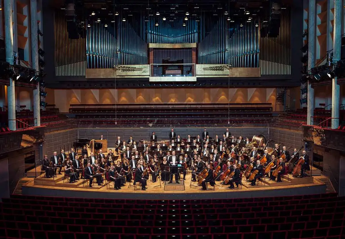 Stor orkester redo för en klassisk musik konsert. En imponerande orgel syns i bakgrunden.