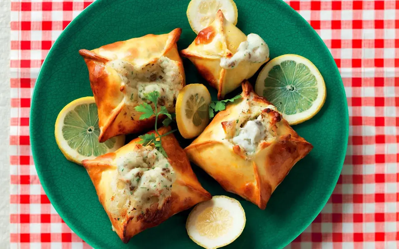 Quattro invitanti secondi di pesce, racchiusi in pasta dorata e guarniti con limone e prezzemolo, su un piatto verde.