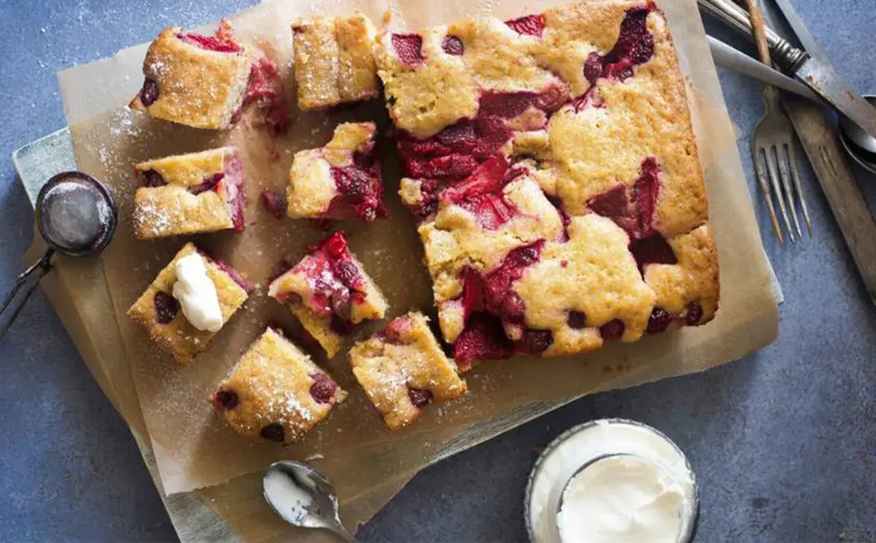 Saftiger Erdbeerkuchen glutenfrei, in St&uuml;cke geschnitten, mit Puderzucker best&auml;ubt und einem Klecks Sahne.