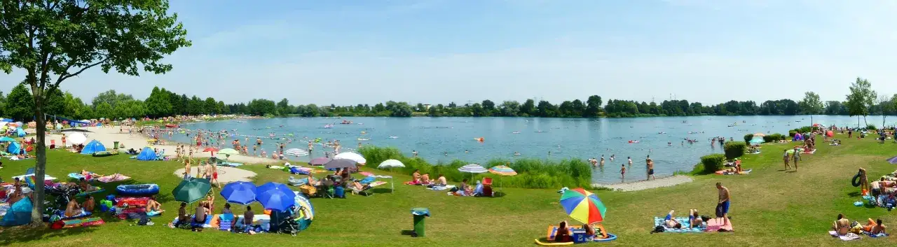 Sommerliche Idylle am Badesee in Deutschland. Menschen entspannen sich am Ufer, schwimmen und planschen im Wasser.