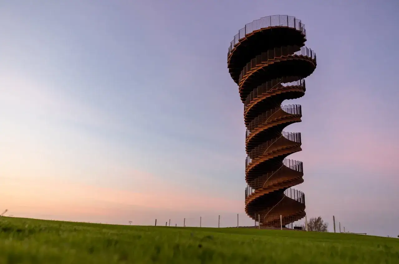 Vridet utsiktstorn i Danmark med spiraltrappa mot en mjukt f&auml;rgad kv&auml;llshimmel.
