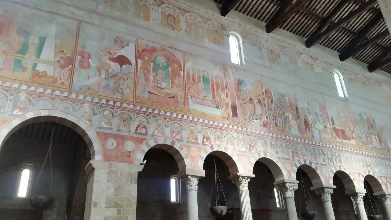 Affreschi medievali narrano storie sacre nella Basilica di San Piero a Grado, con scene bibliche che adornano le pareti sopra le arcate.