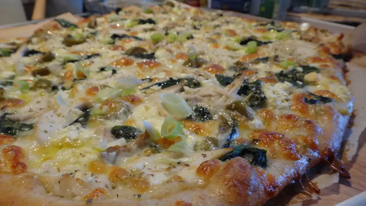 En gyllene spenatpizza med kyckling, fetaost och salladslök, redo att avnjutas.