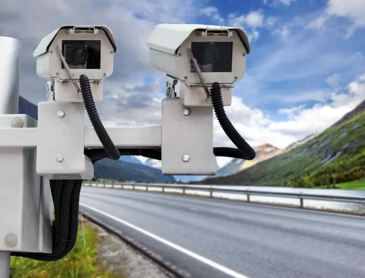 Dos cámaras de **radar de tramo como funciona** en un poste, vigilando una carretera escénica con montañas al fondo.