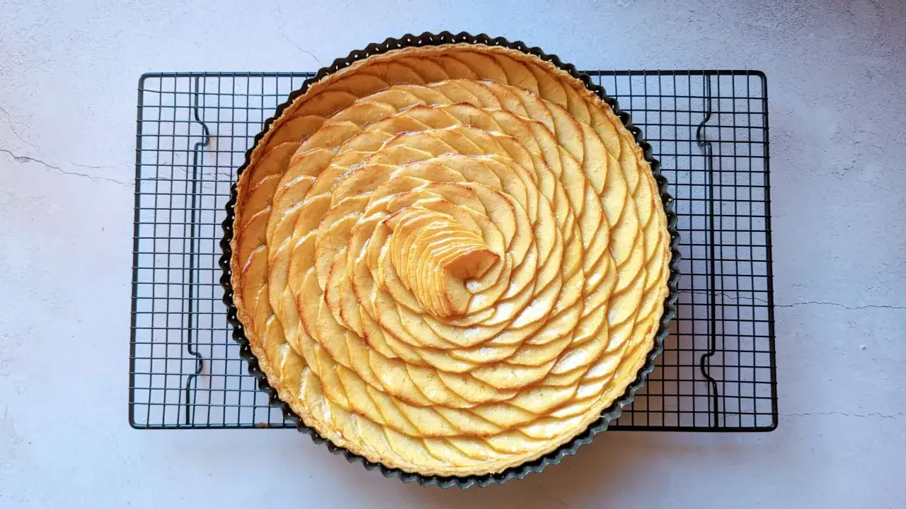Tarte aux pommes magnifiquement décorée de fines tranches de pommes disposées en spirale sur une grille de refroidissement.