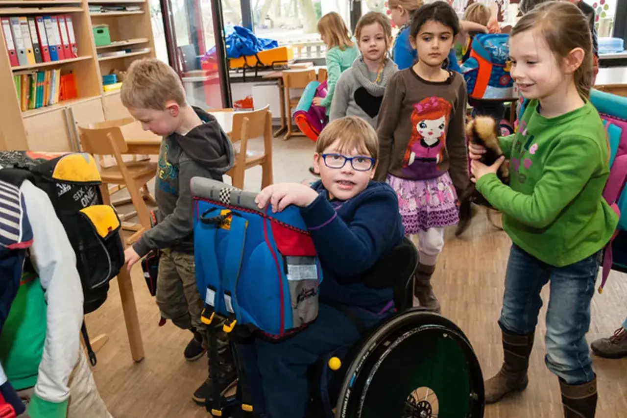Bambini in classe, uno su sedia a rotelle, dimostrano metodologie didattiche inclusive.