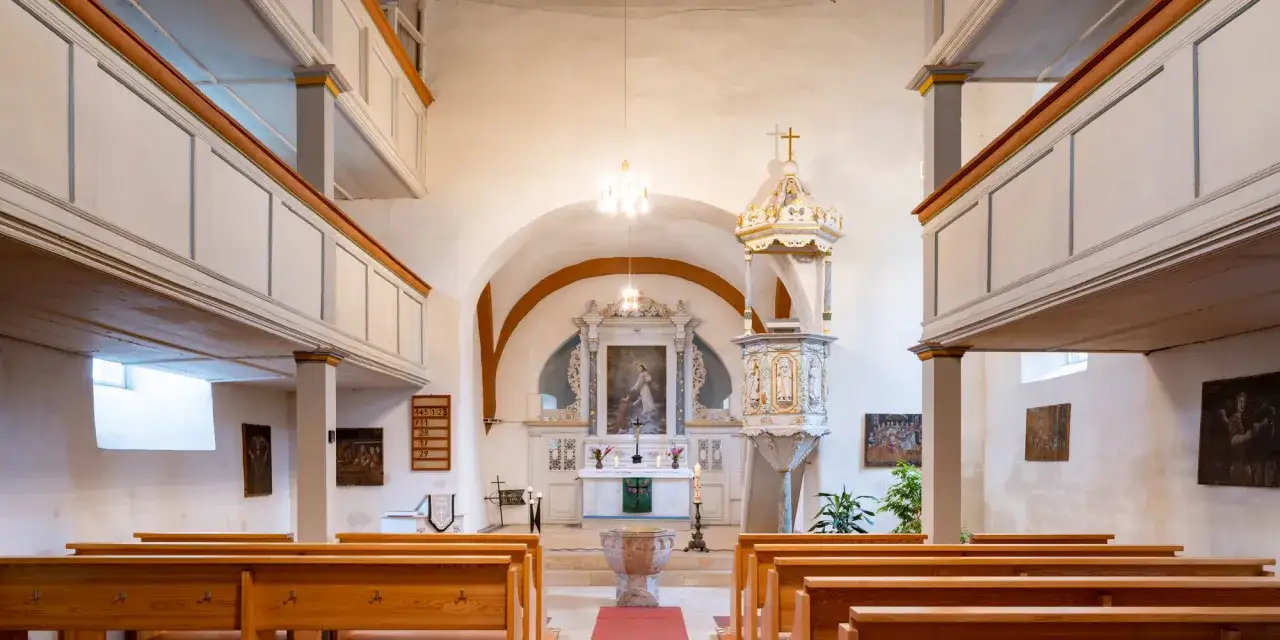 Der Altar der Kirche ist das Herzst&uuml;ck, umgeben von h&ouml;lzernen B&auml;nken und einer Empore.
