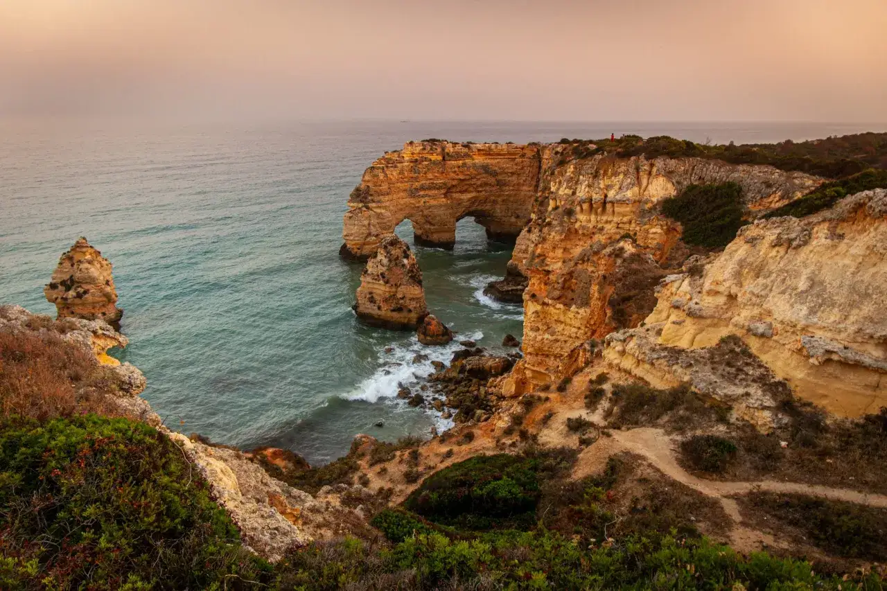 Felsformationen mit Bögen am Meer bei Pera, Portugal. Wellen schlagen gegen die Küste.