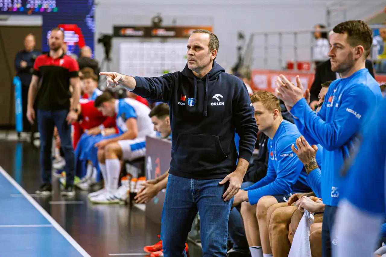 Trener Wisły Płock PSG wskazuje palcem, udzielając wskaz&oacute;wek zawodnikom siedzącym na ławce.