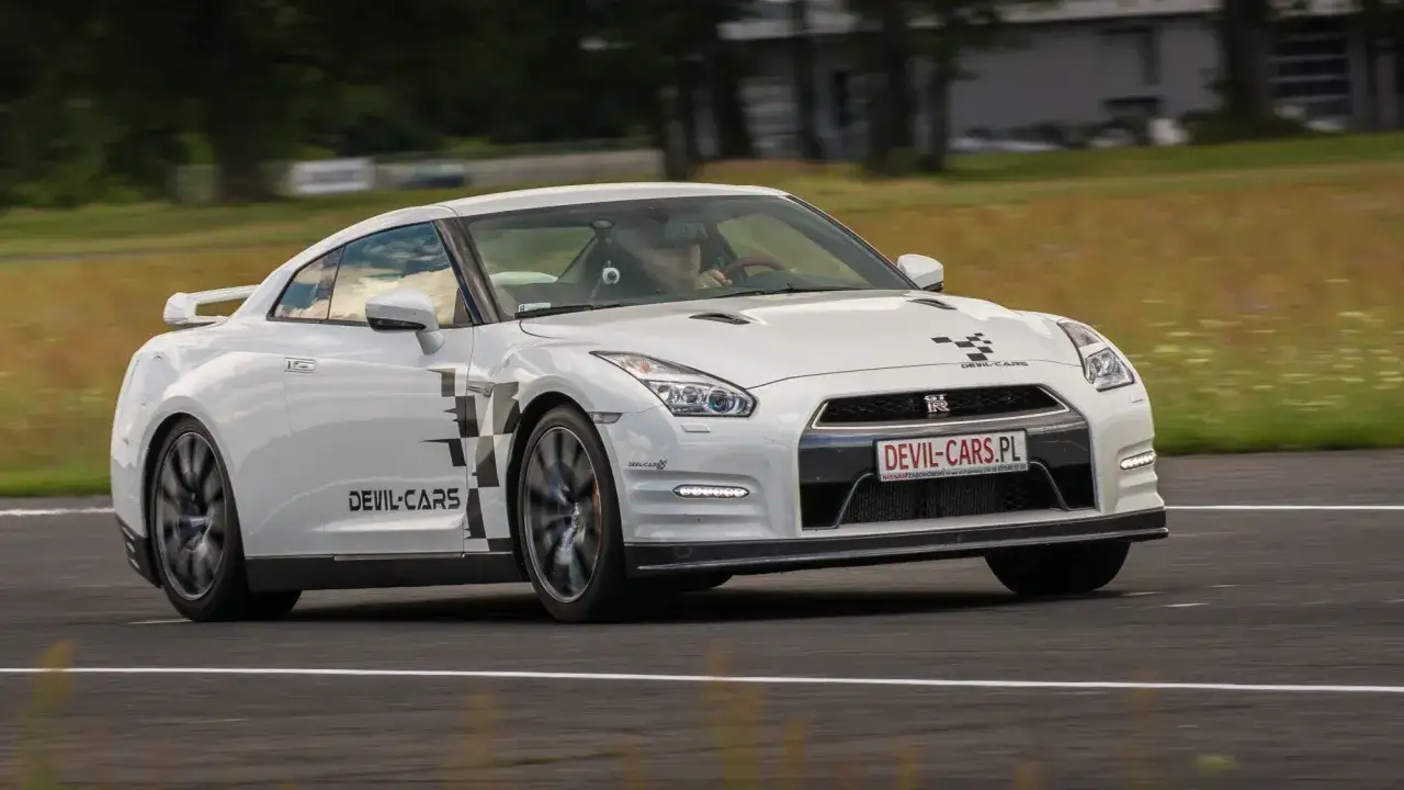 Białe gtr z czarno-białą szachownicą i napisem DEVIL-CARS pędzi po torze wyścigowym.