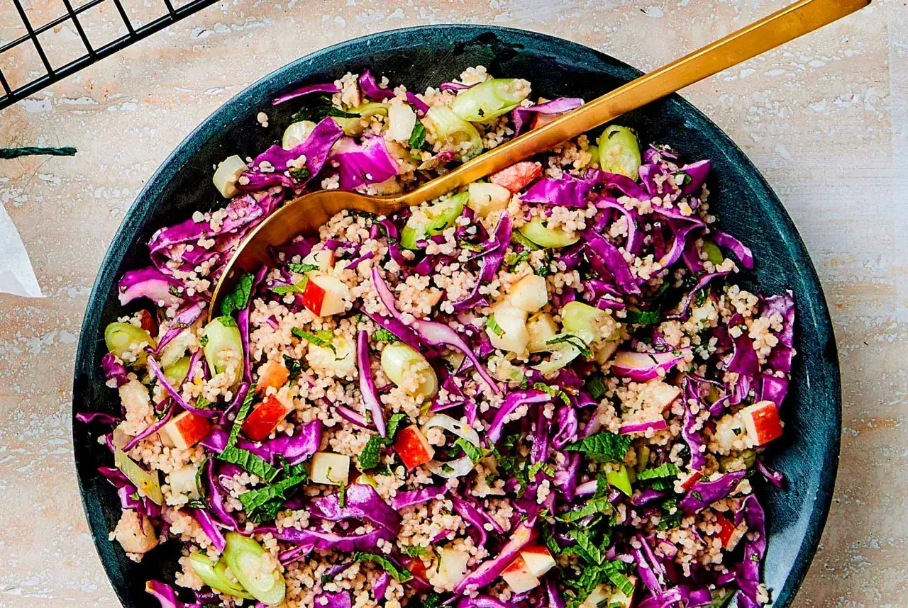 En härlig couscous sallad med rödkål, äpple och mynta. En gyllene sked vilar i den färgglada skålen.