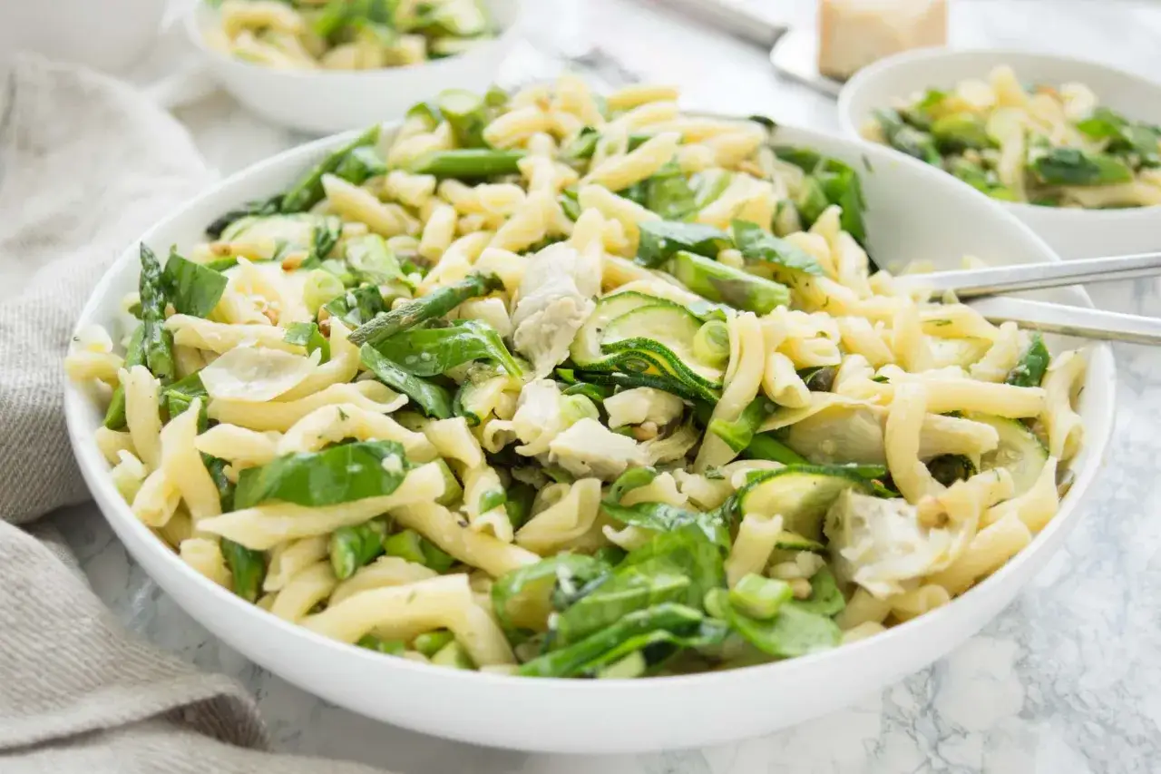 Ein k&ouml;stlicher nudelsalat mit spargel, zucchini und gr&uuml;nen Bl&auml;ttern, serviert in einer wei&szlig;en Sch&uuml;ssel.