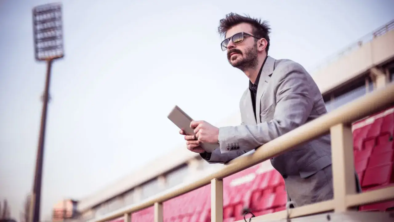 Mann mit Tablet auf Trib&uuml;ne, denkt &uuml;ber sein Sportmanagement Studium in Berlin nach.