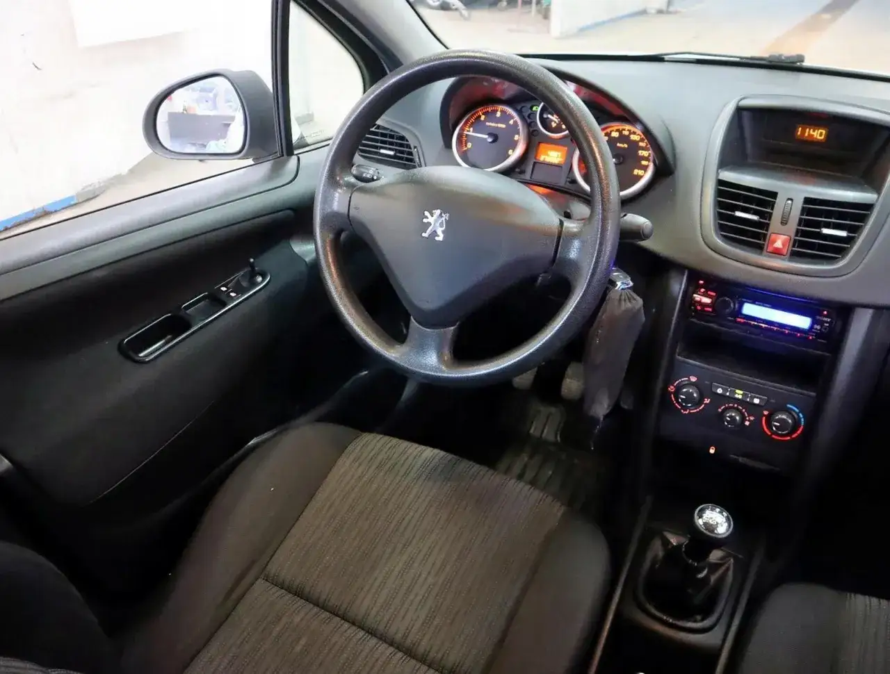 Wnętrze Peugeot 207 1.4 HDI. Widok na deskę rozdzielczą, kierownicę z logo lwa, radio i fotel kierowcy.