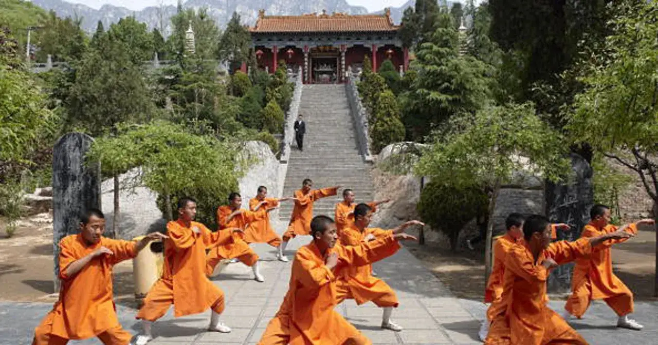 Mnisi w pomarańczowych szatach ćwiczą kung fu przed historycznym klasztorem Shaolin.
