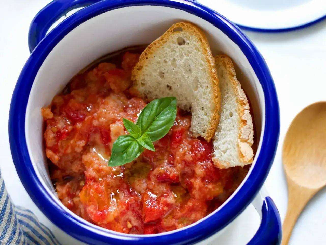 Pappa al pomodoro fumante in ciotola blu, guarnita con pane tostato e basilico fresco. Un piatto confortante e saporito.