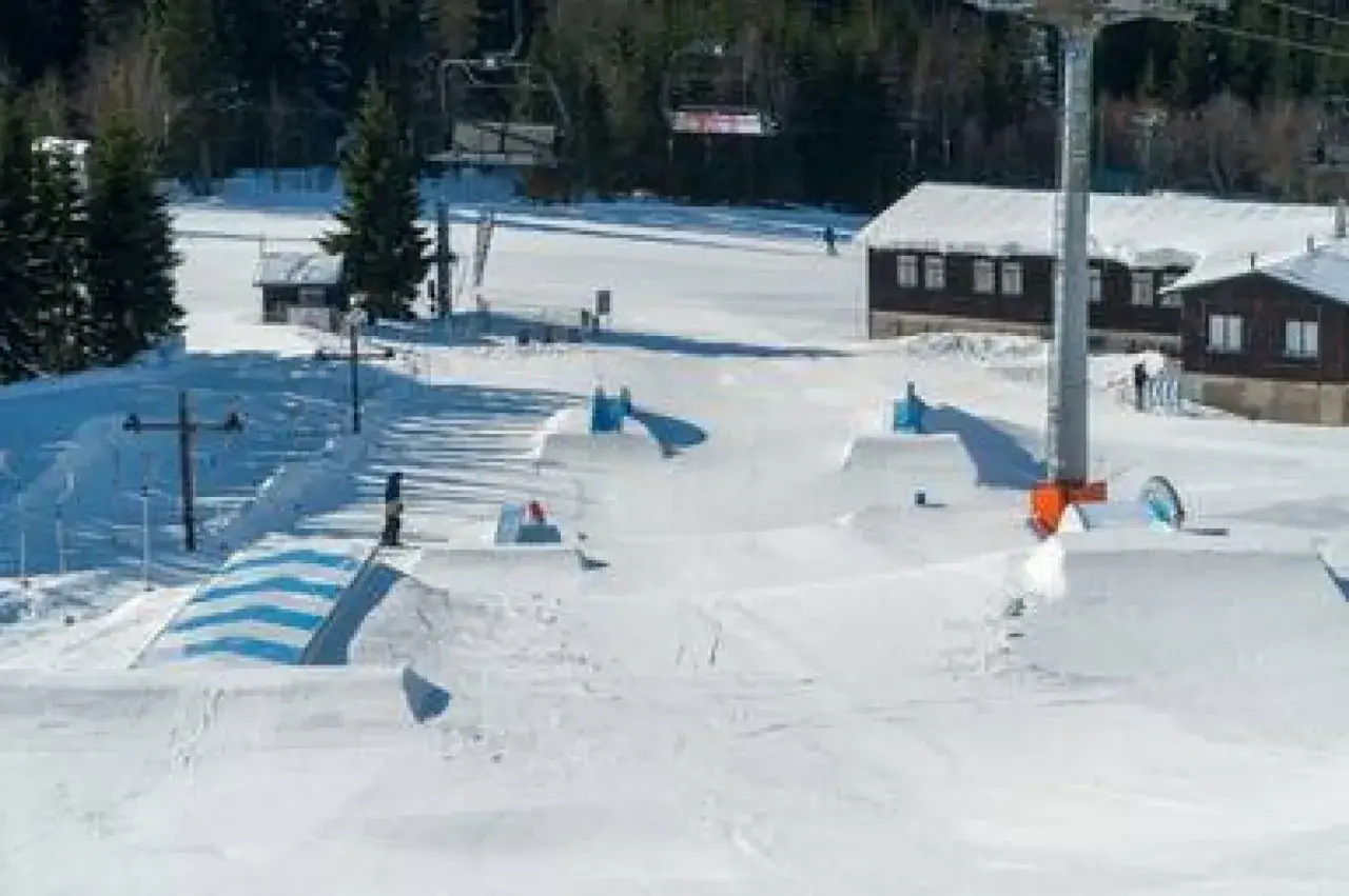 Zimowy dzień w **Špindlerův Mlýn snowparku**. Widoczne liczne skocznie i przeszkody, gotowe na akcję snowboardzistów i narciarzy.