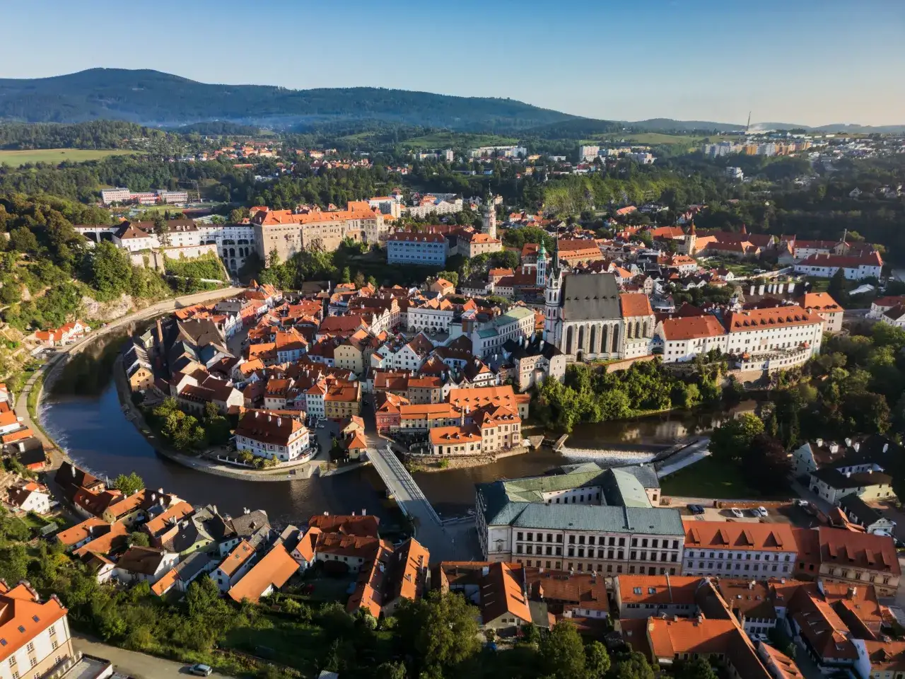 Widok na malowniczy Czeski Krumlov, gdzie rzeka Vltava otacza zabytkowe centrum. Widać zamek, kościół i urokliwe kamienice. To idealne miejsce na odkrywanie czeskich atrakcji.