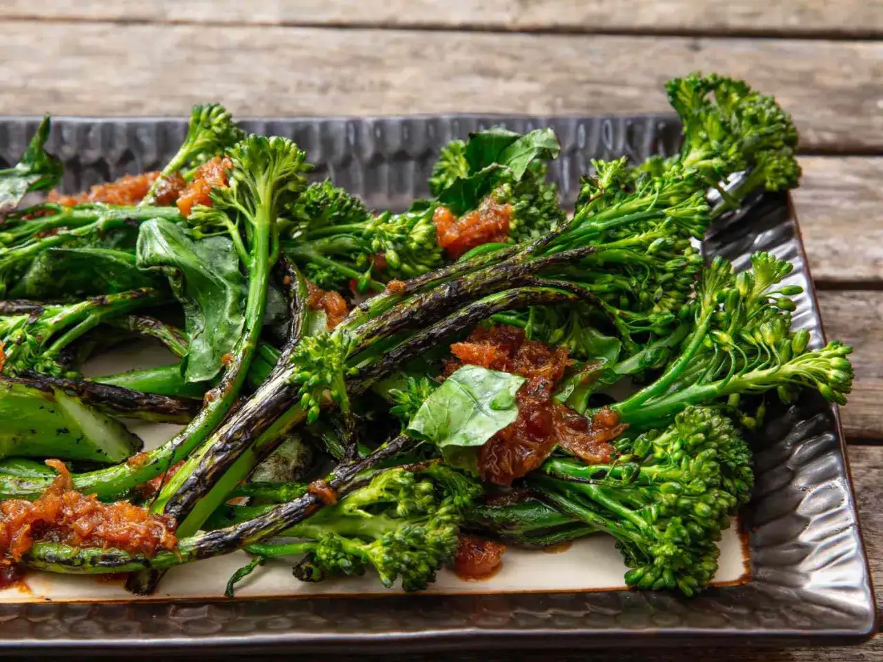 Broccolini grillé, un accompagnement barbecue parfait, servi sur un plat noir avec une garniture orangée.