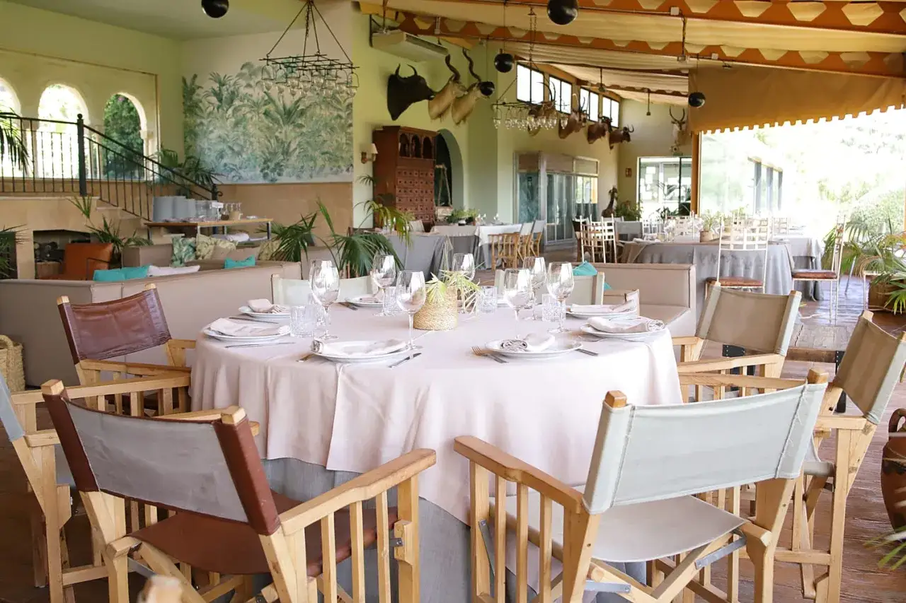 Elegante sal&oacute;n con mesas puestas, ideal para celebrar bautizo. Decoraci&oacute;n con plantas y detalles r&uacute;sticos.