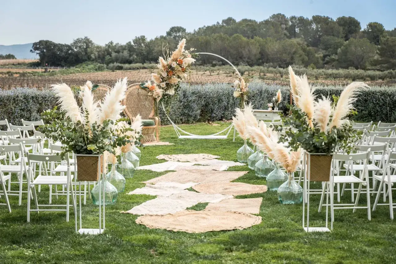 Escenario de boda civil informal con sillas blancas, camino de alfombras de yute, arco floral y pampas. ¡Ideas perfectas para tu gran día!