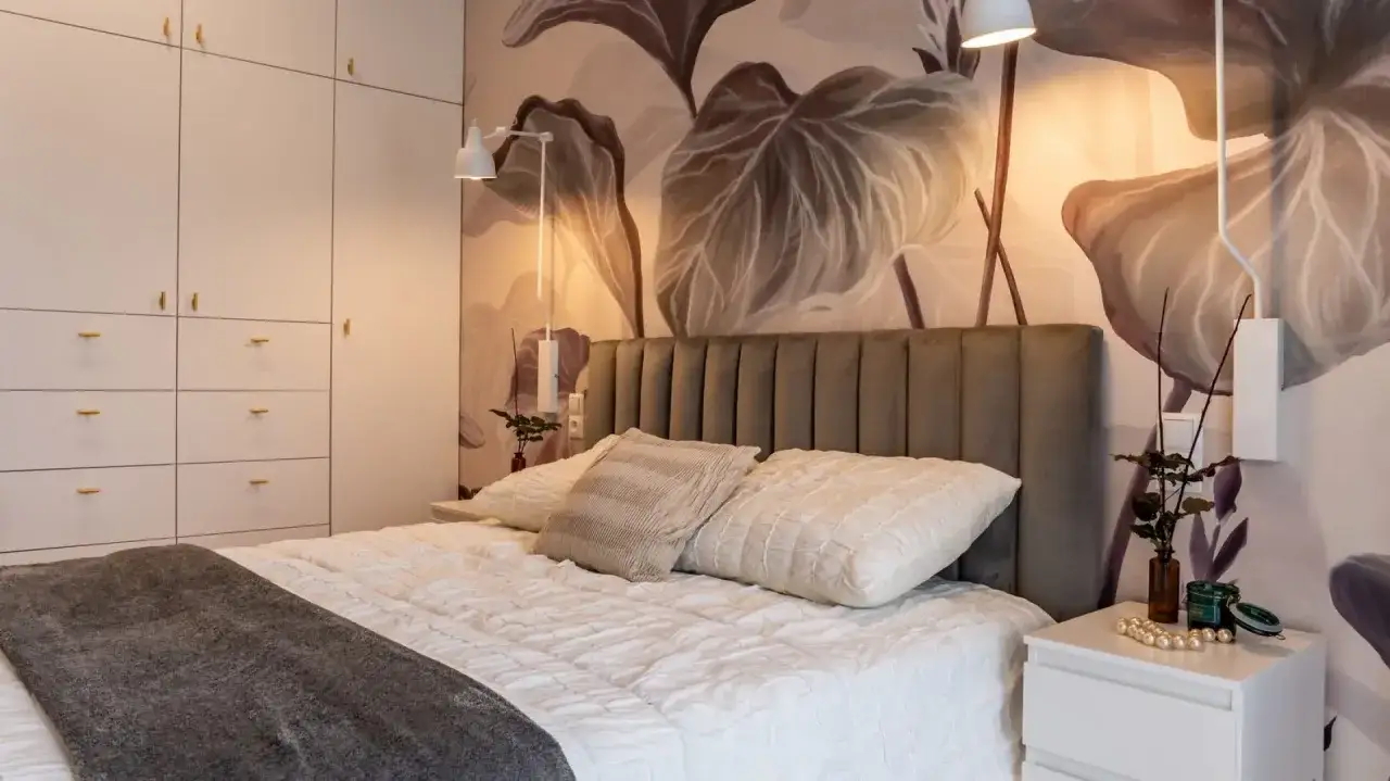 Nowoczesna sypialnia z tapetą w liście, szarą pikowaną ramą łóżka i białymi szafami. Inspiracja, jak urządzić sypialnię w stylu boho-chic.