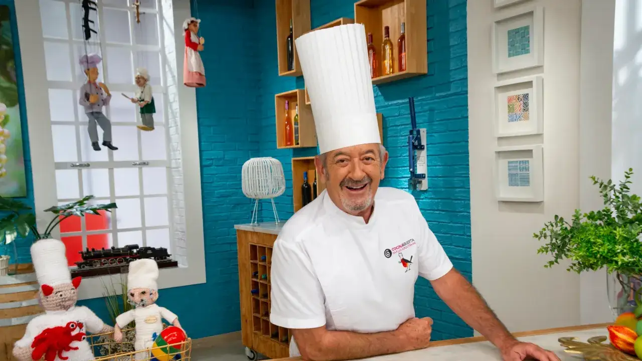 Karlos Argui&ntilde;ano, sonriente con su gorro de chef, en un set de cocina lleno de color y detalles, como marionetas y cuadros.