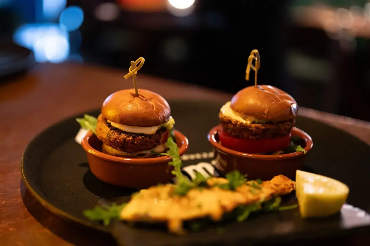 Två små hamburgare, presenterade med passion, som tapas. En klyfta citron och en bit friterad mat ligger framför.