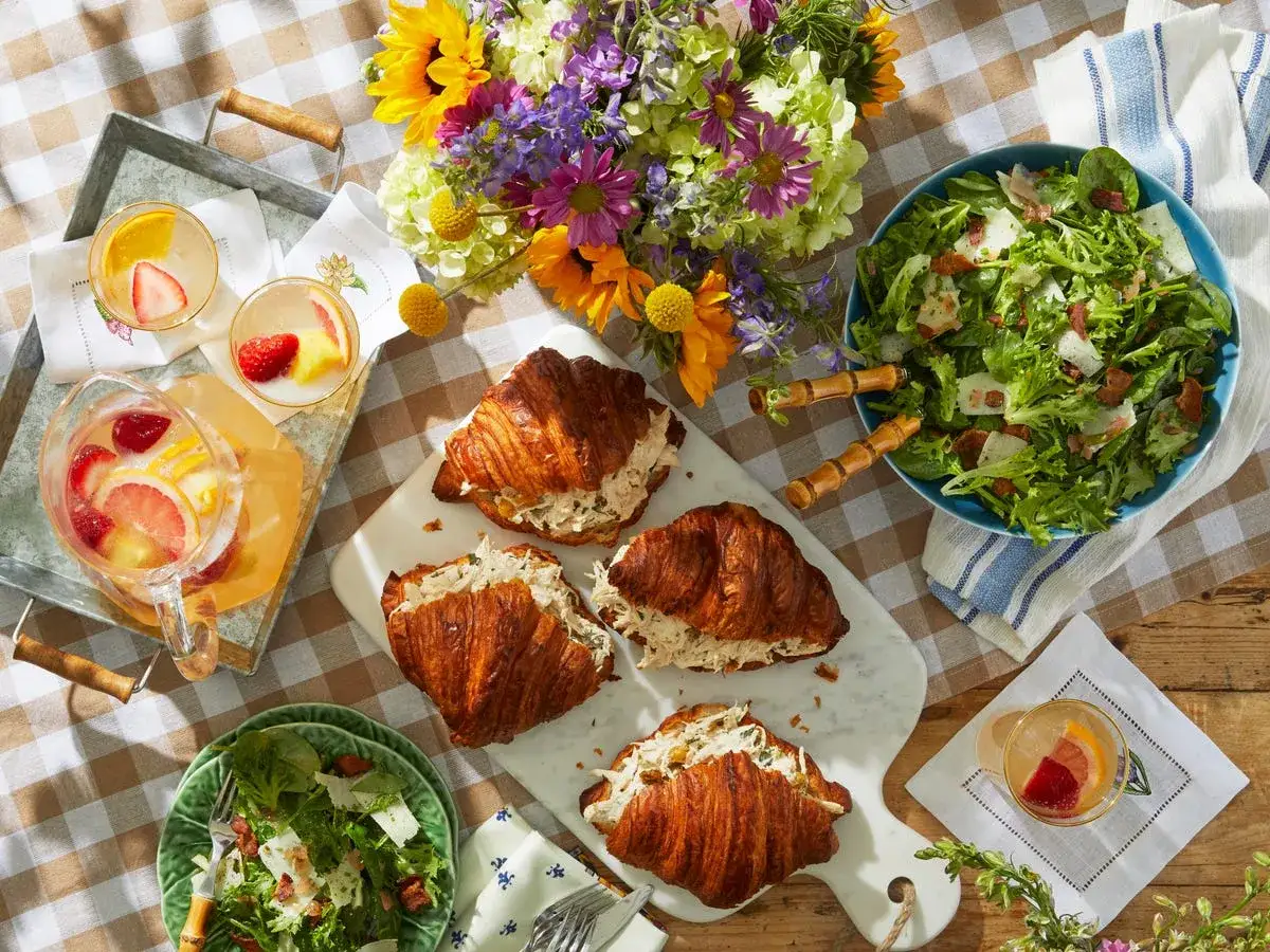 Ein Picknick mit Croissants, Salat und erfrischenden Getränken, perfekt für warmes Wetter.