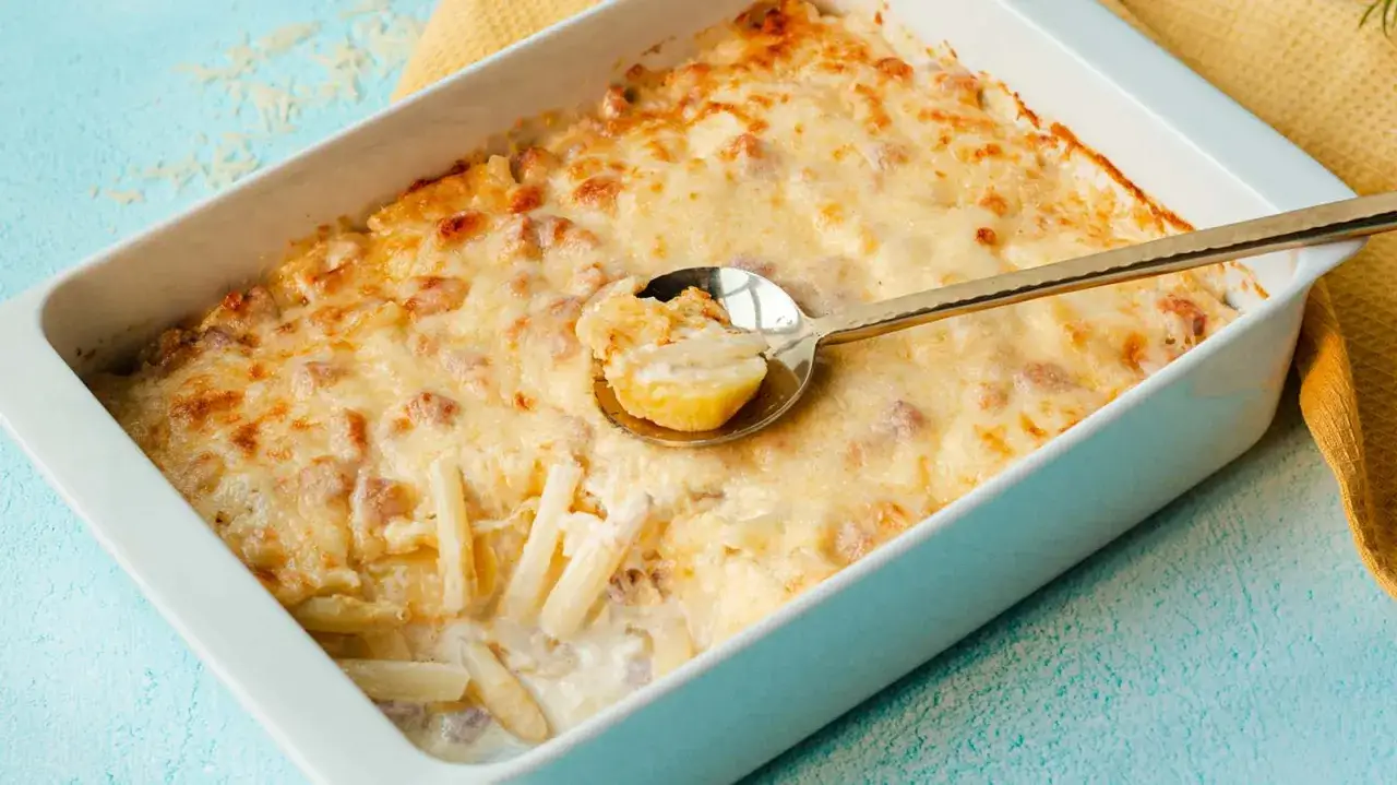 Ein goldbraun überbackener Spargelauflauf mit cremiger Sauce und Käse, serviert in einer weißen Auflaufform. Eine Löffelprobe zeigt zarte Spargelstücke.