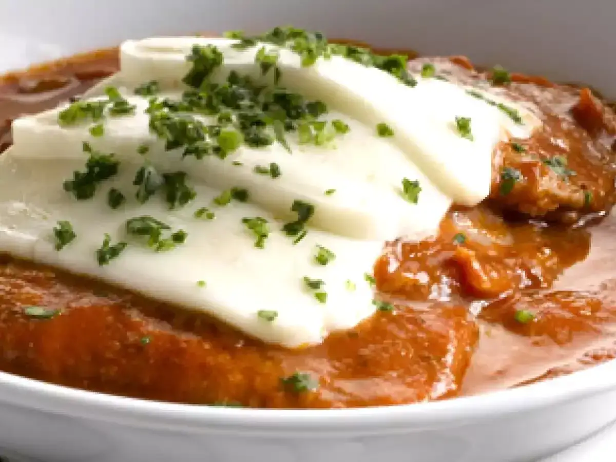 Fettine alla pizzaiola con mozzarella filante, un piatto succulento e invitante, cosparso di prezzemolo fresco.
