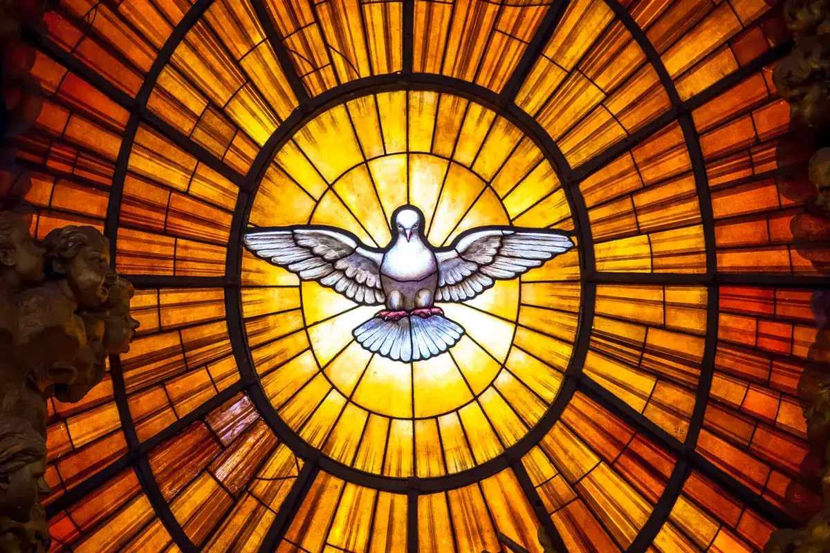 Buntglasfenster mit einer Taube, Symbol des **gottes Geist**, strahlt goldenes Licht aus. Engelk&ouml;pfe flankieren das Kunstwerk.