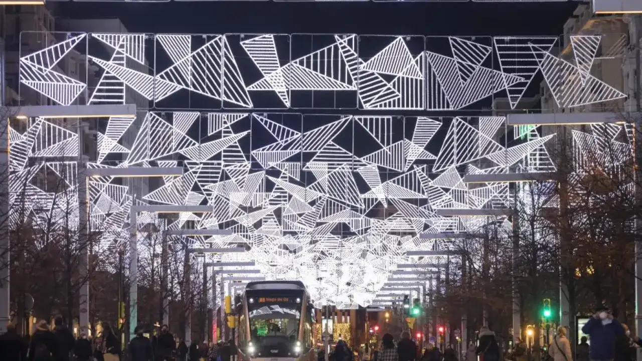El encendido de luces de Navidad en Zaragoza ilumina la calle con un diseño geométrico moderno. Un tranvía avanza entre la gente bajo el espectáculo luminoso.