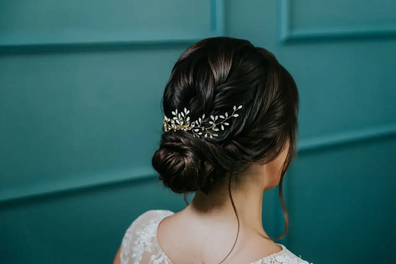 Niski kok w stylu boho z delikatną, złotą spinką z białymi listkami i kryształkami.